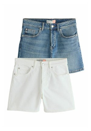 Person trägt weiße Jeansshorts, hat die Hand in der Tasche, draußen mit Grünpflanzen und klarem Himmel im Hintergrund.