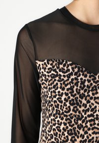 Maglietta nera trasparente a maniche lunghe con un corpetto a stampa leopardata. Il corpetto presenta un collo a cuore e una superficie liscia.