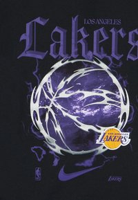 Μαύρο μπλουζάκι με γραφικό μια μοβ μπάλα του μπάσκετ με ασημένιες λεπτομέρειες, περιβαλλόμενη από αστραπές και το κείμενο "Los Angeles Lakers".