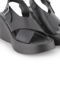 Sandalias de plataforma negras con parte superior de cuero suave, que presentan un diseño de tiras cruzadas y hebilla lateral ajustable. Suela de goma gruesa.