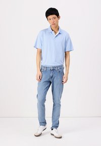 Camisa polo de manga corta de color azul claro con un cuello clásico, combinada con jeans ajustados de lavado claro y zapatillas blancas con acentos grises.