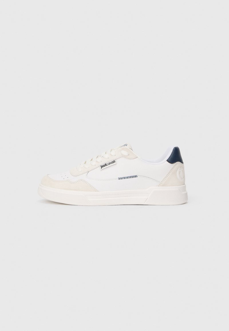 Baskets basses blanches avec des accents en daim beige, languette de talon noire, lacets blancs et étiquette "just cavalli" sur le côté sur un fond gris clair.