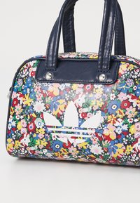 Bolso de mano con estampado floral hecho de material sintético, con asas azul marino, que presenta un logo blanco prominente y detalles en hardware plateado.