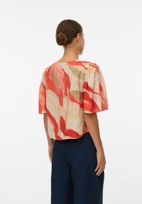 Blouse à manches courtes avec un motif de feuilles abstrait coloré en rouge, beige et vert. Tissu léger à coupe ample et détails plissés.