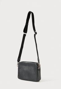 Μαύρη δερμάτινη crossbody τσάντα με ρυθμιζόμενο ιμάντα, κλείσιμο με φερμουάρ και ορθογώνιο σχήμα. Λείο ύφασμα και μινιμαλιστικός σχεδιασμός.