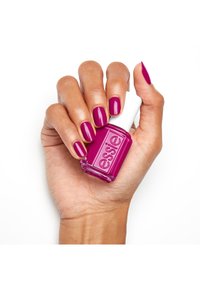 Vernis à ongles fuchsia éclatant dans un flacon en verre transparent avec un capuchon blanc, tenu par une main mettant en valeur des ongles manucurés de la même couleur.