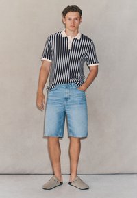 Gestreiftes Poloshirt in Marineblau und Weiß mit Kragen, kombiniert mit hellblauen Jeansshorts und grauen Schuhen. Einfaches und lässiges Design.