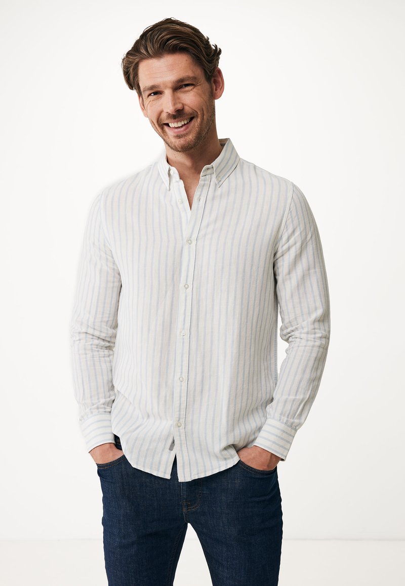 Camisa de botones a rayas en blanco y azul claro, de mangas largas con puños ajustables, combinada con jeans oscuros, de textura suave.