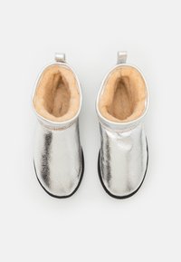 Botine metalice argintii la glezna, cu un exterior neted, căptușeală moale bej și tălpi negre. Dispun de o buclă pentru o purtare ușoară.