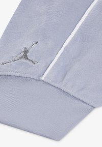 Svijetlosive trenirke s mekanom teksturom, s aplikacijom srebrnog izvezenog Jumpman loga i bijelim trakama sa strane.