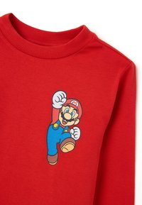 Rotes Sweatshirt mit einem bedruckten Grafikdesign eines Charakters in blauen Latzhosen und erhobenem Arm. Weicher Stoff mit gerippten Nackendetails.