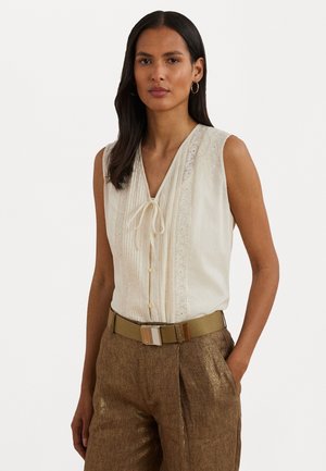Ærmeløs creme bluse med V-hals, teksturerede plisseringer og blonder; parret med høj talje, glitrende bronzebukser og et beige bælte.