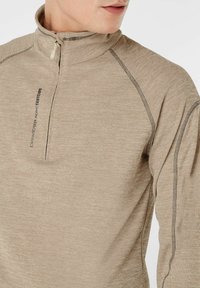 Hellbraunes Zip-Fleece-Pullover mit Stehkragen, strukturiertem Stoff und kontrastierenden dunklen Nähten entlang der Nähte und Schultern.
