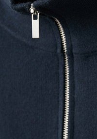 Námořnický oděv na zip s vysokým límcem, zdobený stříbrným kovovým zipem a texturovanou látkou, s jemnými detaily a těsným střihem.