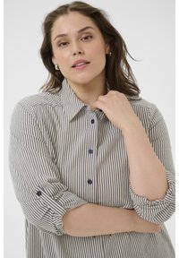 Chemise à rayures crème et marine avec col classique, manches retroussables et boutons foncés, offrant une coupe décontractée.