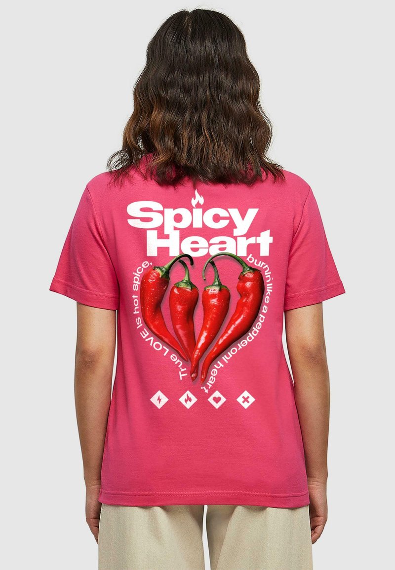 Camiseta de algodón rosa con un gráfico de tres pimientos rojos en forma de corazón, rodeado de texto y símbolos en blanco.