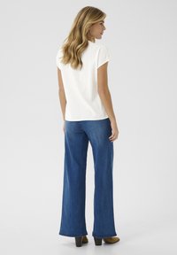 Un top alb cu mânecă scurtă asociat cu blugi evazați albaștri. Ținuta are un croi lejer și o textură uniformă, cu un design de culoare solidă.
