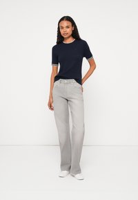 Ναυτικό ριμπ πλεκτό πουλόβερ κοντομάνικο με άσπρες λεπτομέρειες, συνδυασμένο με ανοιχτό γκρίζο φαρδύ τζιν παντελόνι. Το μοντέλο στέκεται σε ουδέτερο φόντο φορώντας άσπρα παπούτσια.