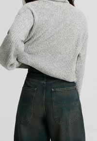 Pull gris côtelé à la coupe ample, associé à un jean en denim foncé taille haute avec deux poches arrière et des détails de couture.