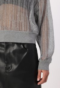 Srebrny sweter z siateczki z szarymi ściągaczami na mankietach i u dołu, zestawiony z czarnymi spodniami z ekologicznej skóry z detalem przedniej kieszeni.