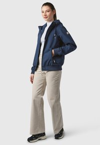 Marinblå vindjacka med dragkedja fram, snörning i huvan, sidofickor och ribbade ärmslut. Matchas med ljusbeiga byxor och sneakers.