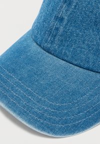 Καπέλο από τζιν σε ανοιχτό μπλε χρώμα, με καμπυλωτό γείσο και αντιθετική ραφή. Υφασμάτινη επιφάνεια με ομοιόμορφο φινίρισμα και ενισχυμένες ραφές.
