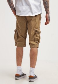 Shorts cargo khaki avec de grandes poches latérales, une coupe décontractée et des ourlets retroussés. Fabriqués à partir d'un tissu léger avec des détails de couture visibles.