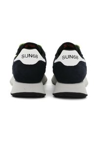 Baskets en suède bleu marine avec des bouts de talon blancs et des accents vert lime. Elles présentent des semelles grises épaisses et des crampons noirs. La marque sur les talons indique "SUN68."