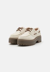Sapatos de couro bege com bico arredondado, atacadores castanhos e uma sola plataforma castanha robusta com padrões de ranhura profundos.