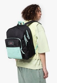 Zaino nero con accenti verde menta; presenta spallacci regolabili, molteplici scomparti e una tasca anteriore in rete. Tessuto resistente e design strutturato.