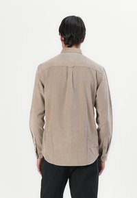 Long-sleeve shirt in light brown corduroy, featuring a back yoke, side vents, and buttoned cuffs. Smooth texture with vertical stripes.