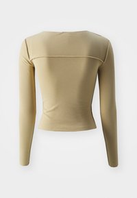 Långärmad, åtsittande topp gjord av slät beige tyg. Har en rundad halsringning och horisontell sömdetalj över ryggen.