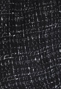 Tessuto tweed bianco e nero con una trama testurizzata, caratterizzato da un motivo a griglia e occasionali fili bianchi per il contrasto.