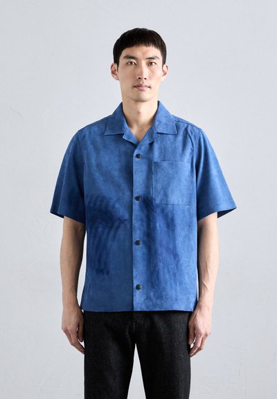 Chemise bleu à manches courtes en matériau semblable à du daim, dotée d'une poche sur la poitrine et de boutons noir. Couleur uniforme avec une texture douce.