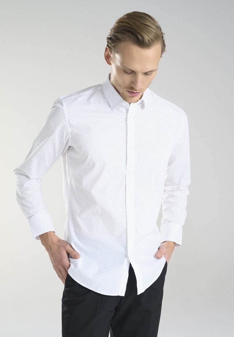 Biała koszula z długim rękawem, zapinana na guziki, z małymi czarnymi kropeczkami oraz z wysmuklonym kołnierzykiem. Wykonana z gładkiego materiału o dopasowanym kroju.