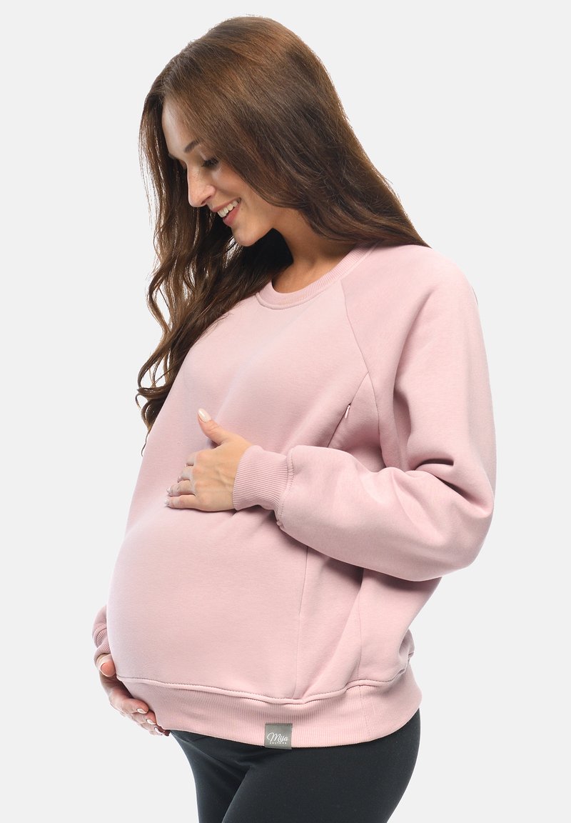 Felpa per maternità rosa con maniche lunghe, scollo rotondo e vestibilità comoda. Presenta polsini e orlo a costine, con un dettaglio di tasca laterale.