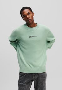 Mintgrøn strikket sweater med rund hals, ribbet manchetter og bund, med "KARL LAGERFELD JEANS" broderet i sort på forsiden.