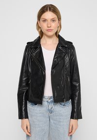 Černá kožená motorkářská bunda se zipovými kapsami, límečkem a přiléhavým střihem. Nositá přes bílý top, spárovaná se světle modrými džíny.