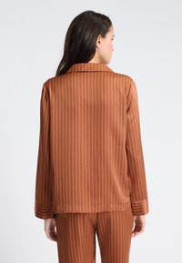 Brązowa marynarka w paski z różowymi liniami, dopasowany krój, długie rękawy i klapa, w komplecie ze spodniami w tym samym wzorze. Gładka faktura.