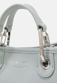 Jasnoniebieska skórzana torebka o fakturowanej powierzchni, ze srebrnymi okuciami i grawerowanym logo na boku. Posiada zaokrąglone uchwyty i ozdobne elementy metalowe.