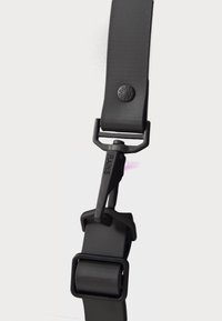 Correa negra con hebilla y clip ajustable, con un logotipo y textura suave, sobre un fondo blanco.