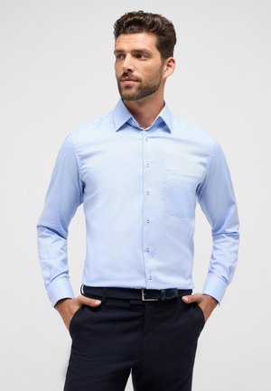 Himmelblaues Langarmhemd mit Button-Down-Kragen, einzelner Brusttasche und subtiler Textur, kombiniert mit dunklen Hosen und einem geflochtenen Gürtel.