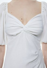 Weißes Kleid aus Leinenmischung mit quadratischem Ausschnitt und geknotetem Frontdetail. Verfügt über Puffärmel und drapierte Seiten. Glatte Textur.