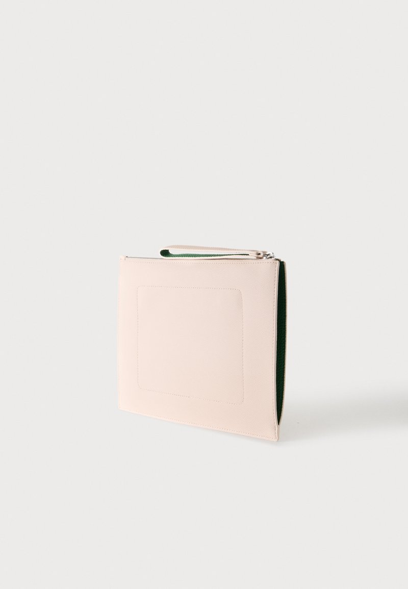 Beige rechteckige Clutch mit Handgelenksriemen und Reißverschluss, aufrecht stehend vor hellem einfarbigem Hintergrund.