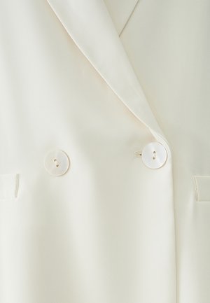 Kreemikasus kahe rinna nööpidega, sileda tekstuuriga, millel on kaks suurt ümmargust valget nööpi ja küljetaskud.