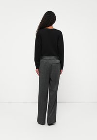 Zwarte lange mouwen top gecombineerd met hoog geplaatste, geplooide grijze broek met een gestructureerd patroon en een strakke achterzakdetail.