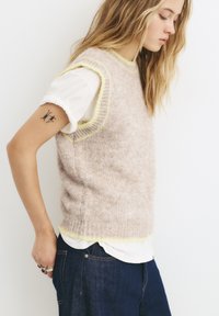 Helles rosa ärmelloses Strickpullover mit gelbem Besatz; weiche Textur; über einer weißen Bluse getragen; zu dunkelblauen Jeans kombiniert.