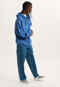 Sudadera de algodón azul con un bolsillo frontal, combinada con jeans de corte holgado y zapatos de lona de cuadros en blanco y negro.