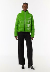 Groene pufferjack met hoge kraag, glanzende afwerking, gestikt ontwerp, voorrits en drukknoopsluitingen, gecombineerd met zwarte wijde broek.