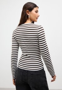 Långärmad topp med horisontella bruna och vita ränder; figurnära design med en slät textur. Bärs med mörka, högmidjade jeans.